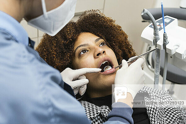 Female patient looking up while receiving treatment from dentist during pandemic at clinic
