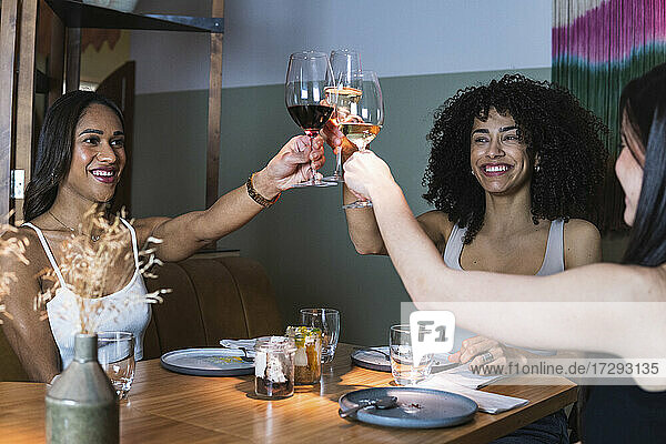 Glückliche Frauen stoßen mit Weingläsern während einer Party im Restaurant an