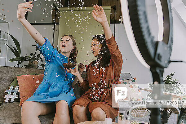 Cheerful women celebrating with confetti while filming at home
