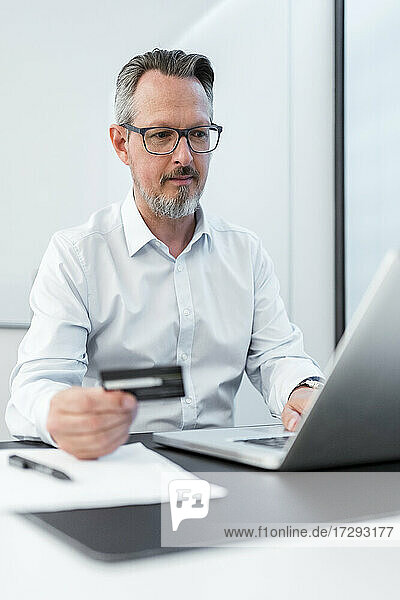 Männlicher Unternehmer mit Kreditkarte und Laptop im Büro