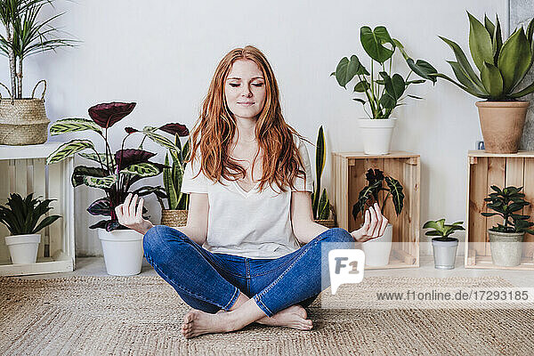 Rothaarige Frau meditiert  während sie zu Hause auf dem Boden sitzt