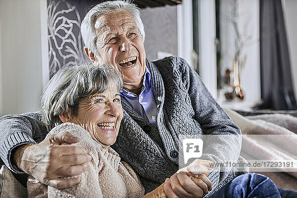 Älteres Paar hält sich an den Händen  während es zusammen im Wohnzimmer sitzt