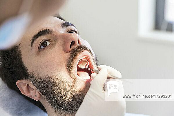 Zahnärztin mit angewinkeltem Spiegel bei der Untersuchung der Zähne eines männlichen Patienten in einer medizinischen Klinik