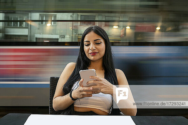 Junge Frau  die ein Mobiltelefon benutzt  während sie in der Dämmerung an einem Tisch in einem Cafe sitzt