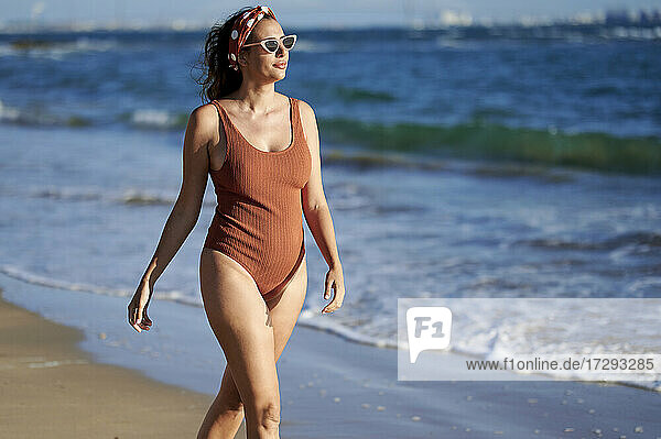 Frau im Badeanzug schaut weg  während sie am Strand spazieren geht