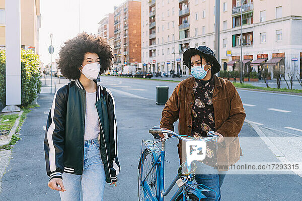 Freundinnen mit Schutzmasken auf dem Fahrrad auf der Straße