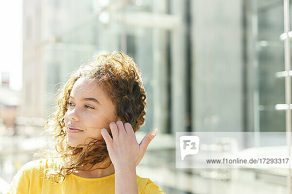 Beautiful woman adjusting curly hair on sunny day