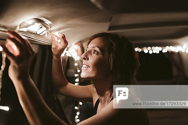 Lächelnde Frau  die nachts Lichter in einem Lieferwagen anbringt