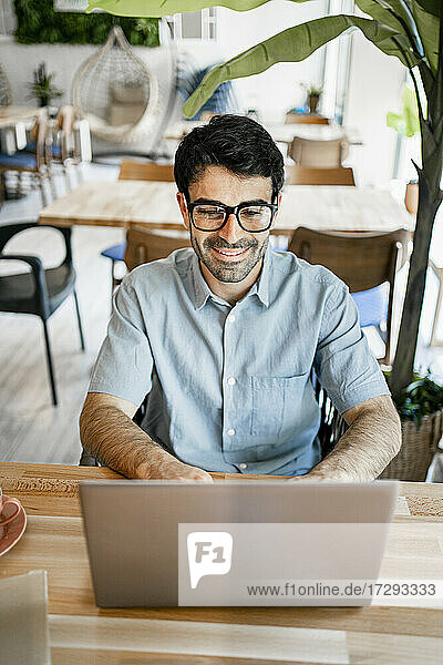 Smiling young businessman using laptop at table in cafe