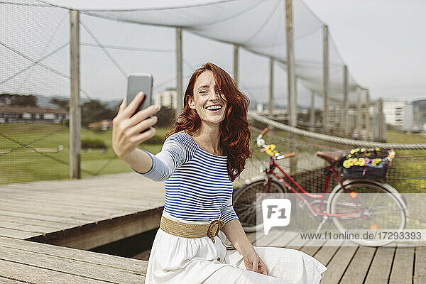 Frau  die ein Selfie mit ihrem Smartphone macht  während sie auf dem Pier sitzt