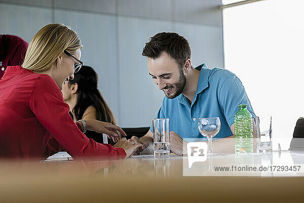 Lächelnder männlicher und weiblicher Fachmann  der ein digitales Tablet mit einer weiblichen Kollegin im Hintergrund im Büro benutzt