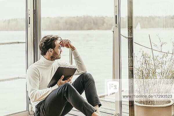 Geschäftsmann schaut weg  während er mit einem digitalen Tablet in einem Hausboot sitzt