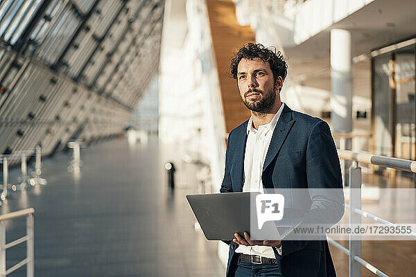 Männlicher Unternehmer mit Laptop  der wegschaut  während er in der Büro-Lobby steht