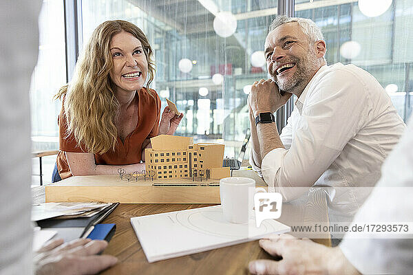 Lächelnde männliche und weibliche Architekten  die einen Kollegen ansehen  während sie am Schreibtisch im Büro diskutieren