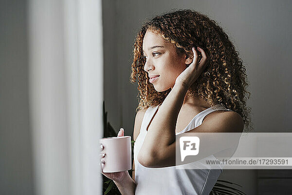 Schöne Frau mit Hand in den Haaren schaut weg  während sie im Schlafzimmer Kaffee trinkt