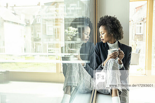 Weibliche Fachkraft schaut nach unten  während sie auf der Fensterbank im Büro sitzt