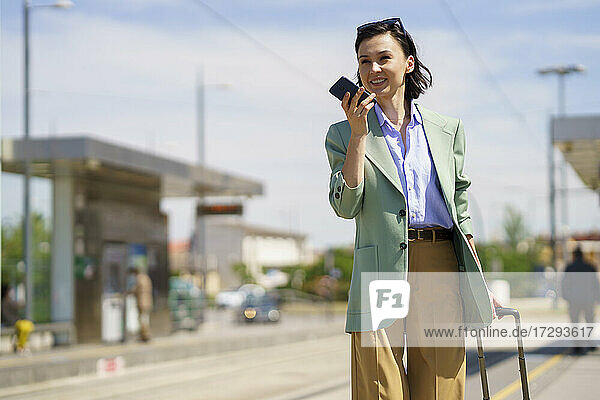 Geschäftsfrau sendet Sprachnachricht über Smartphone am Bahnhof