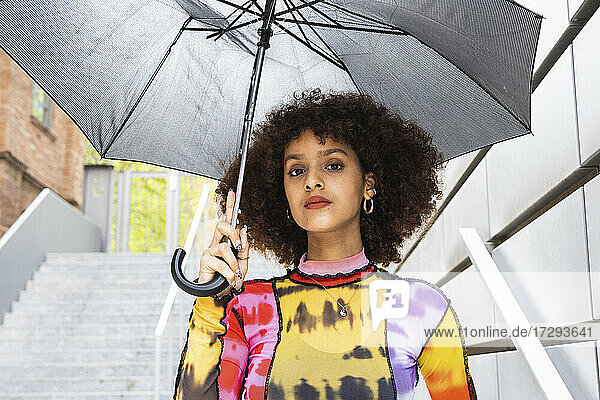 Junge Frau mit lockigem Haar  die einen Regenschirm hält und starrt