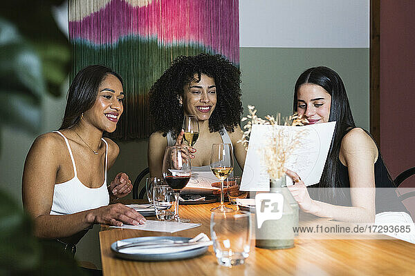 Frau zeigt Freunden die Speisekarte  während sie in einem Restaurant etwas trinkt