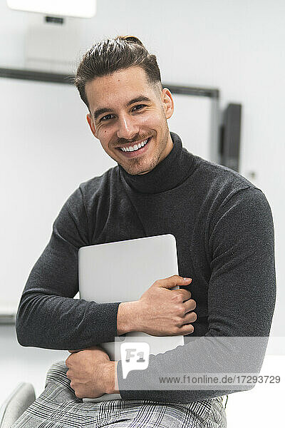 Lächelnder junger Geschäftsmann mit Laptop im Büro
