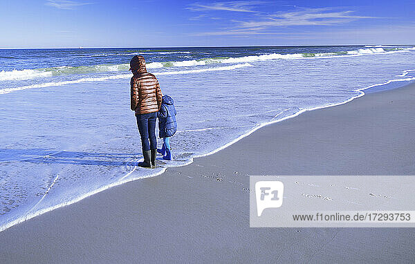Mother with daughter standing on shore at beach