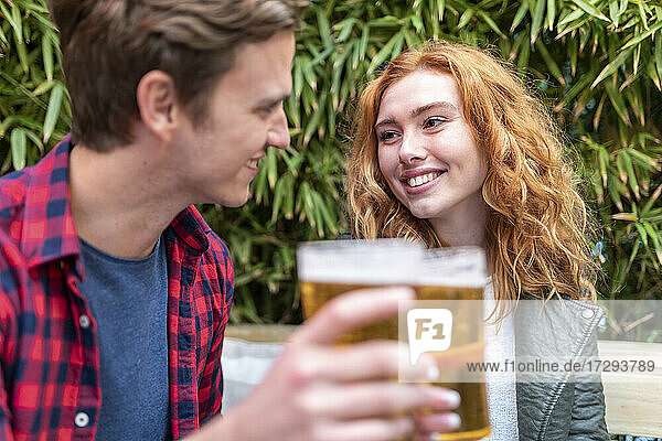 Lächelnde Frau sieht ihren Freund an  der in einer Kneipe ein Bierglas hält