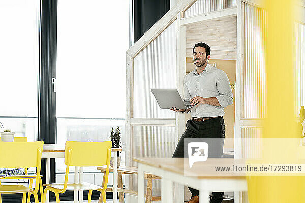 Männlicher Unternehmer  der seinen Blick abwendet  während er in der Cafeteria einen Laptop in der Hand hält