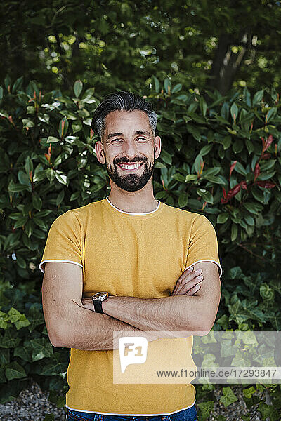 Lächelnder Mann mit verschränkten Armen vor Pflanzen stehend