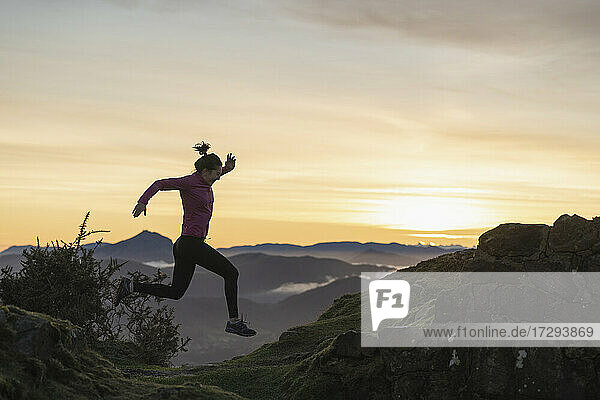 Junge Frau springt beim Laufen während des Sonnenaufgangs