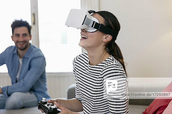 Young woman laughing while playing with virtual reality simulator at home
