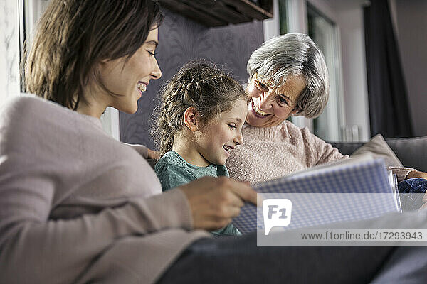 Tochter schaut sich ein Fotoalbum an  während sie mit ihrer Familie im Wohnzimmer sitzt