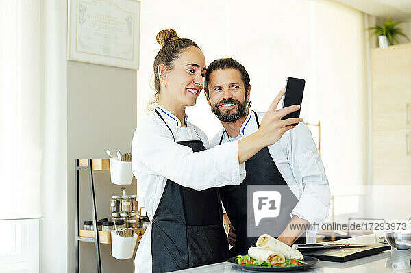 Glückliche Köche machen ein Selfie mit ihrem Handy in der Küche eines modernen Restaurants