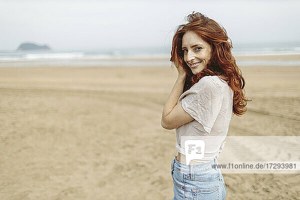 Lächelnde rothaarige Frau am Strand stehend