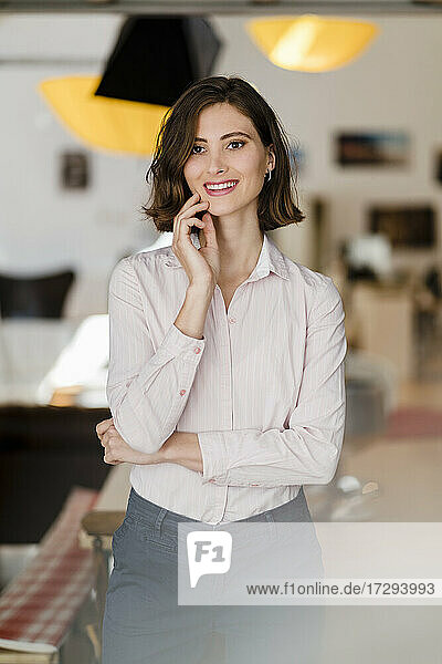 Smiling beautiful female professional with hand on chin standing in office looking away
