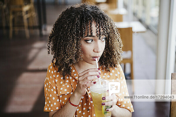 Junge Frau mit lockigem Haar schaut weg  während sie in einem Café Eistee trinkt