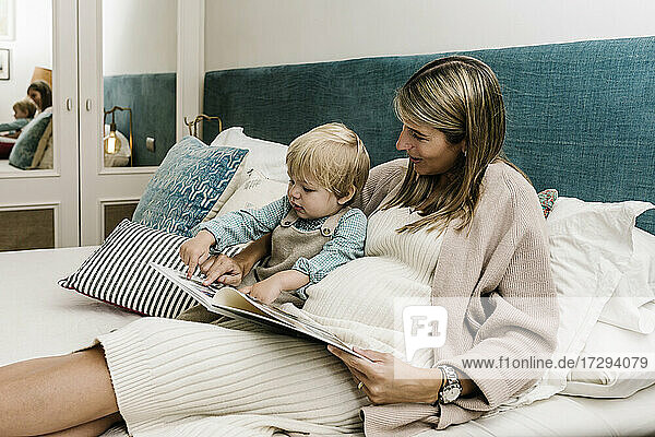 Schwangere Frau zeigt ihrem Sohn ein Fotoalbum  während sie zu Hause auf dem Bett sitzt