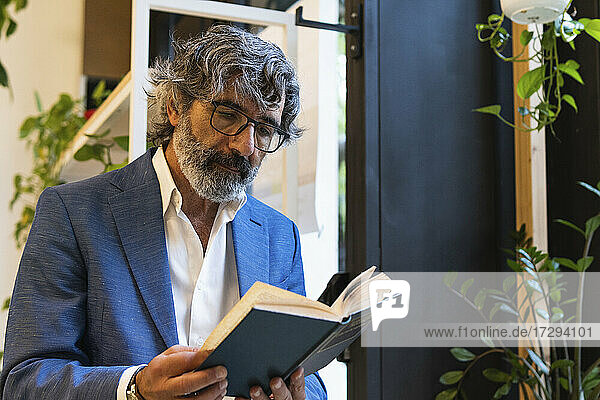 Älterer Geschäftsmann mit Brille liest Tagebuch im Büro
