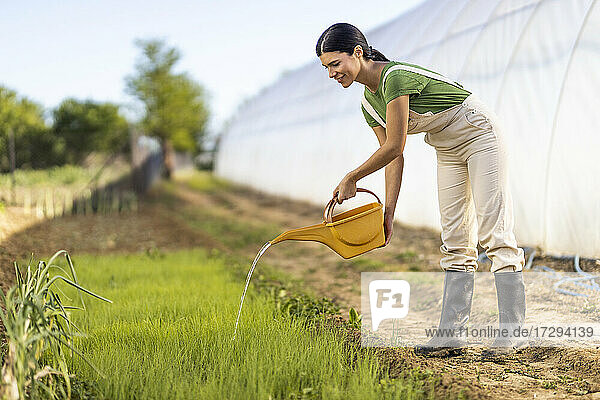 Junge Bäuerin beim Bewässern von Pflanzen auf einem Biohof