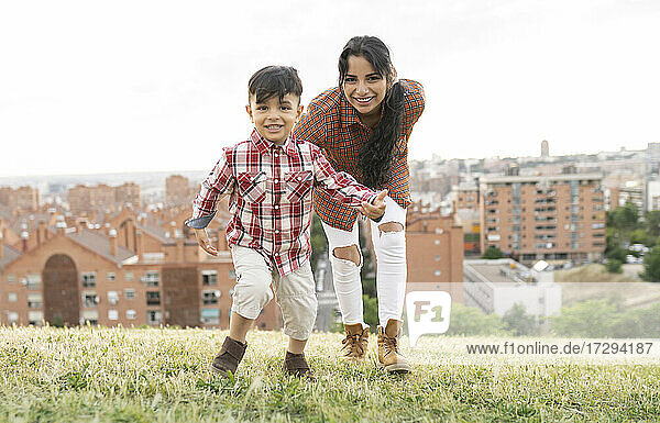 Lächelnde Mutter und Sohn spielen auf einem Hügel mit Stadtlandschaft im Hintergrund