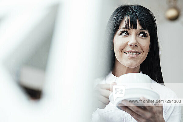 Lächelnde Besitzerin mit Kaffeetasse  die im Café wegschaut
