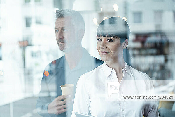 Businesswoman looking away while standing with colleague in background at cafe