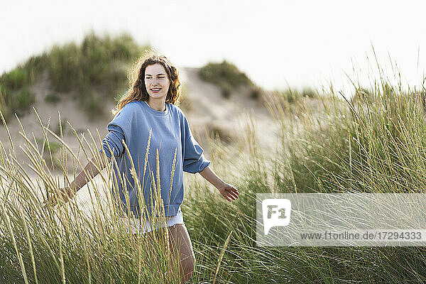 Young woman with arms outstretched walking in dunes