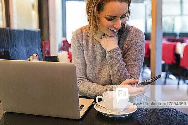 Lächelnde Freiberuflerin mit Handy am Tisch im Café