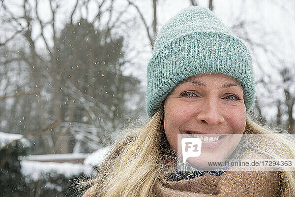 Smiling beautiful blond woman wearing knit hat during snow