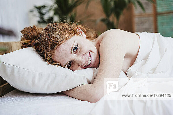 Lächelnde Frau mit Decke auf dem Bett liegend zu Hause