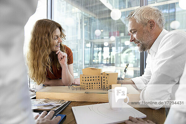 Smiling male and female architect looking at model in office