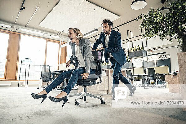 Businessman playing with colleague sitting on office wheel chair