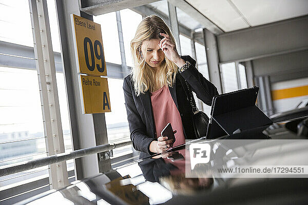 Junge Frau schaut auf einem Parkplatz auf ein digitales Tablet