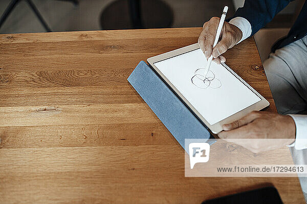 Älterer Geschäftsmann  der im Büro auf einem digitalen Tablet zeichnet