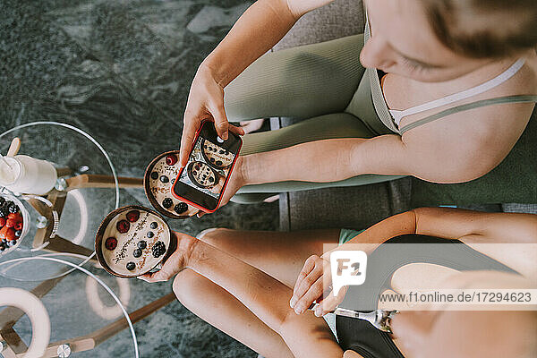 Frauen fotografieren Joghurt-Obstschalen mit dem Smartphone